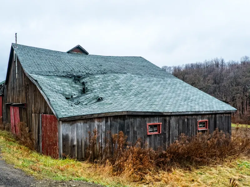 Weathered rural New York barn with a sagging, failing shingle roof — what age and water do over decades