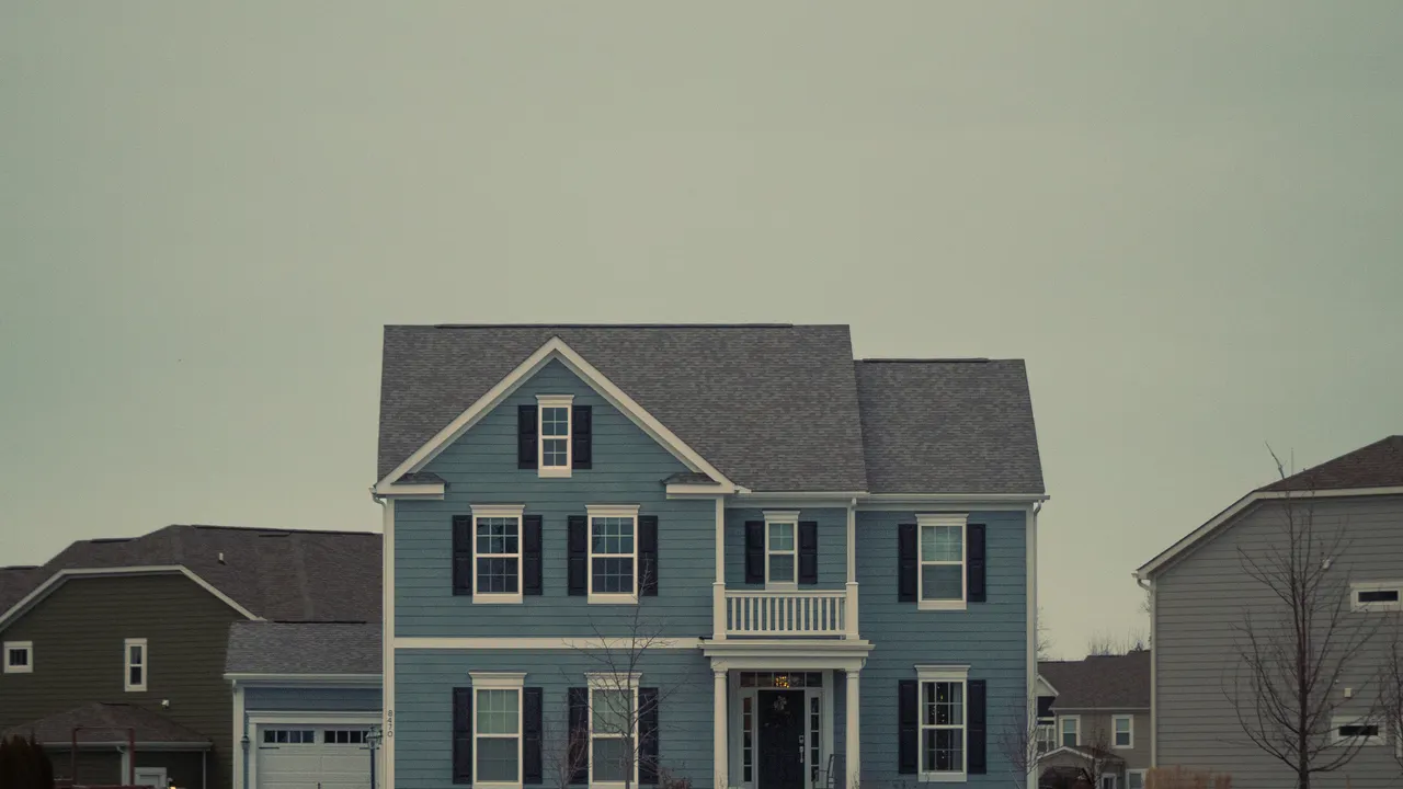 Two-story colonial with gutters and downspouts at every eave under an overcast sky &mdash; representative