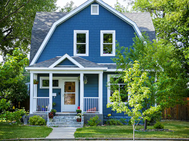 Blue Dutch colonial with gambrel asphalt roof on a leafy village street