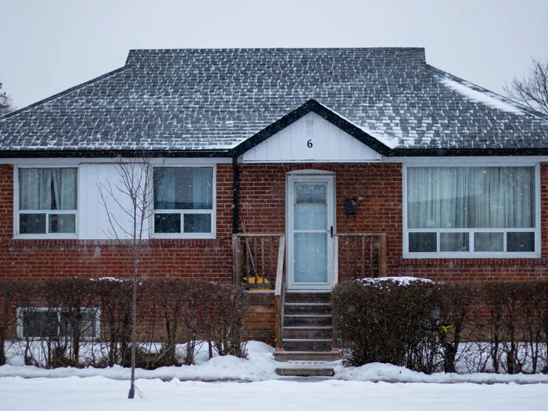 Post-war brick bungalow with snow-dusted hip roof on a quiet winter street