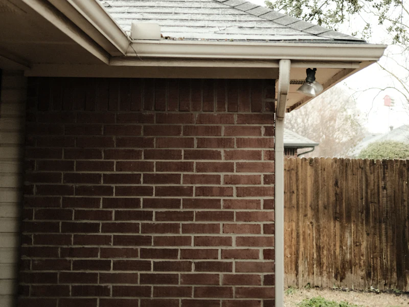Eave detail: gutter, downspout, and soffit line over brick — representative