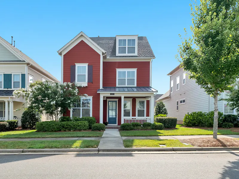 Brick two-story home with brown architectural shingle roof and arched entry under a bright sky