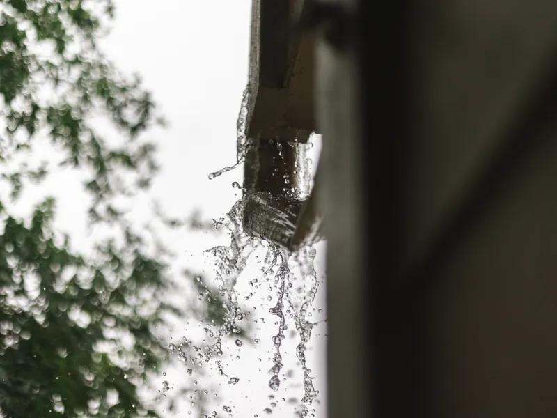Rainwater gushing over a failed gutter corner in a downpour &mdash; representative