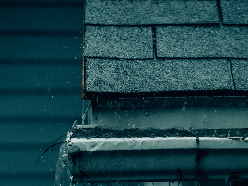 Rainwater overshooting a gutter at the eave during a storm — representative