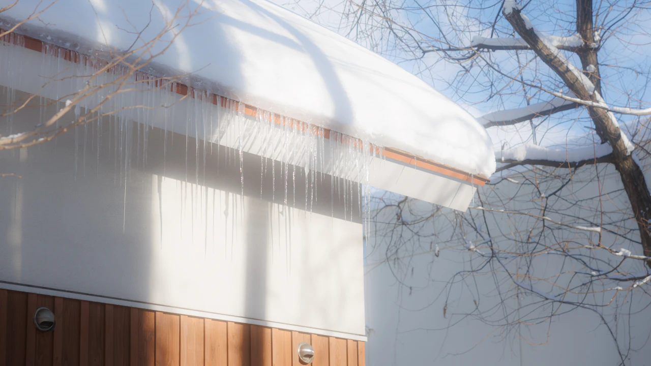 Snow overhanging an eave with a curtain of icicles &mdash; the visible signature of an ice dam