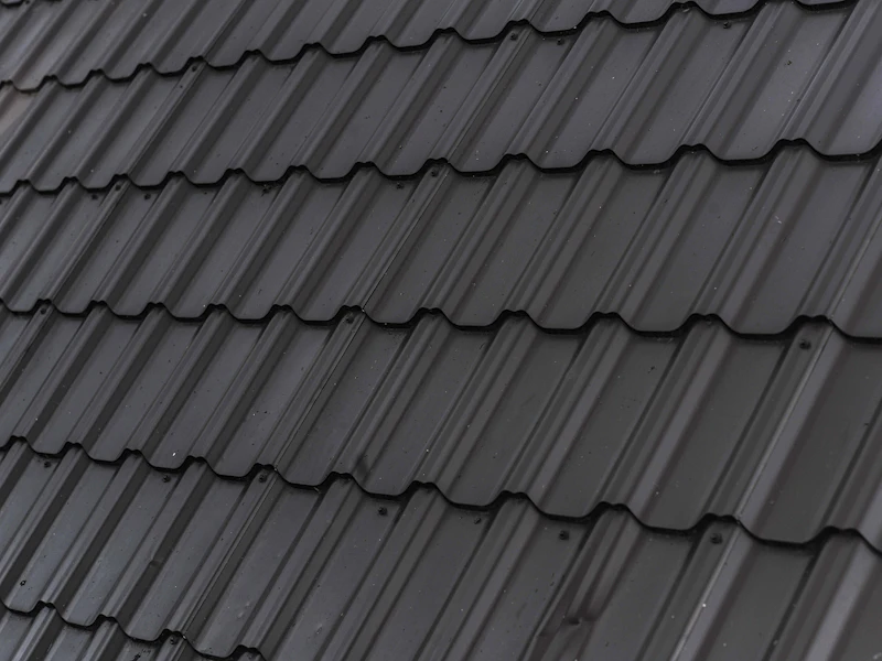 Dark stamped metal roofing panels in close-up, interlocked courses shedding light rain