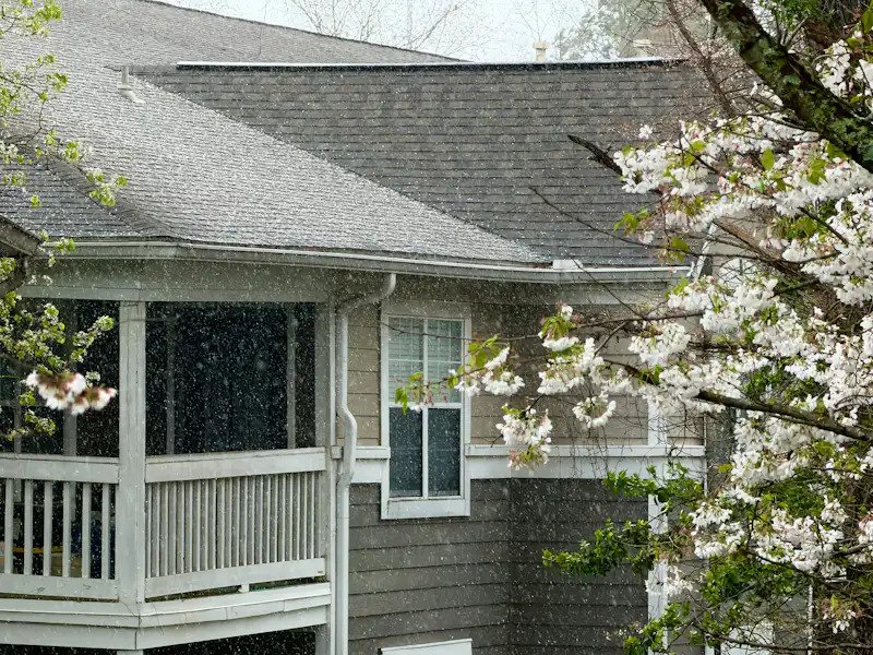 Steady rain streaming across an asphalt shingle roof toward the gutter &mdash; representative