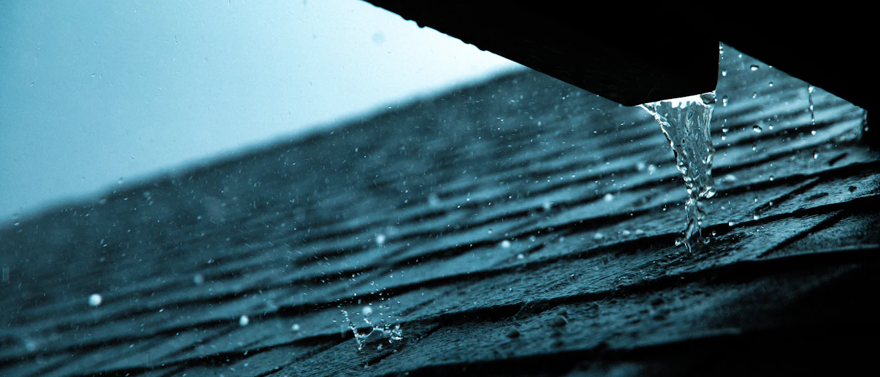 Rain beading and dripping off a shingle roof edge in low storm light