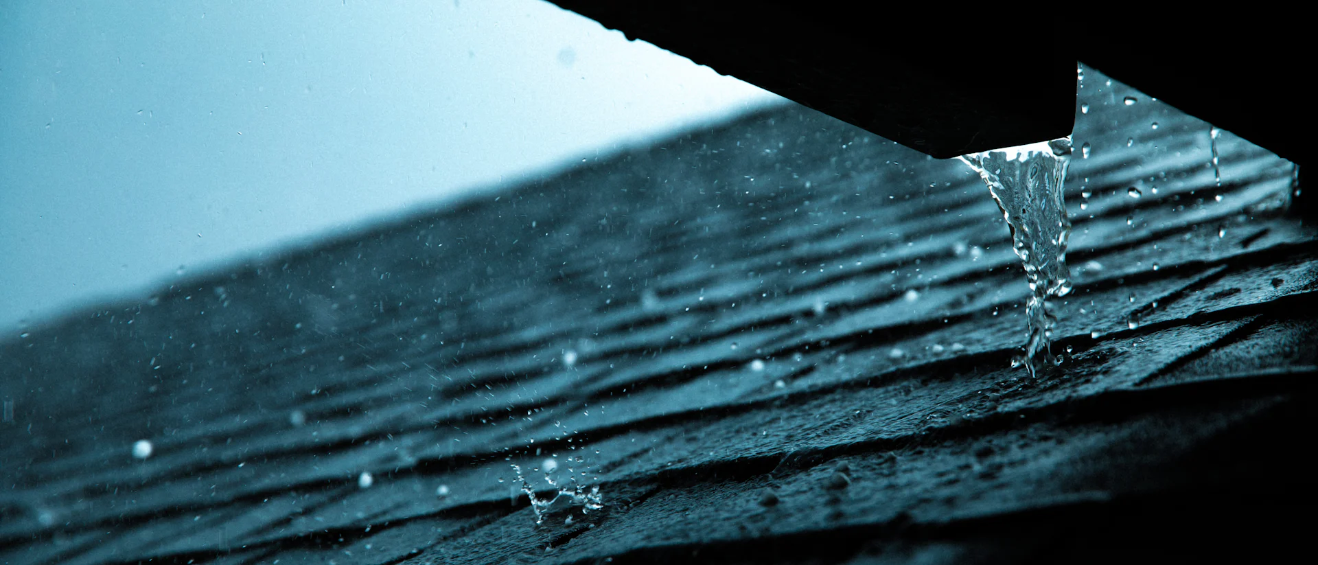 Rain beading and dripping off a shingle roof edge in low storm light