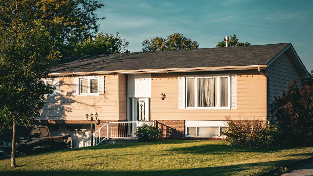 Raised ranch home with dark asphalt shingle roof at dusk, mature tree in the yard