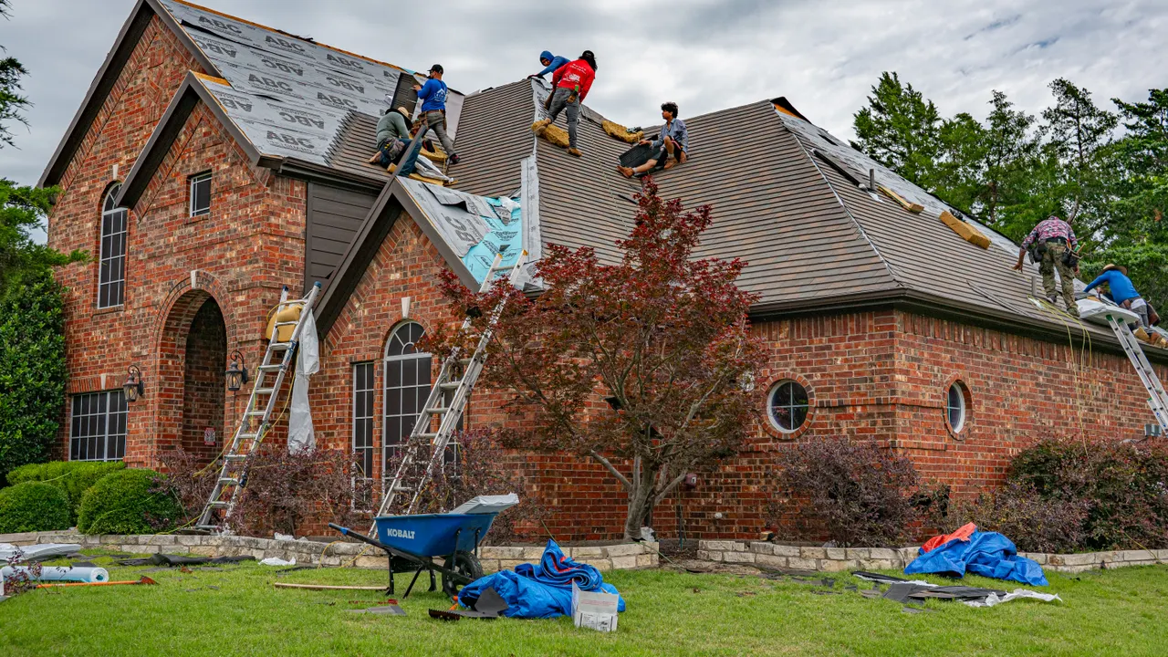 Roof replacement in progress on a brick two-story home, old shingles stripped to the deck — representative