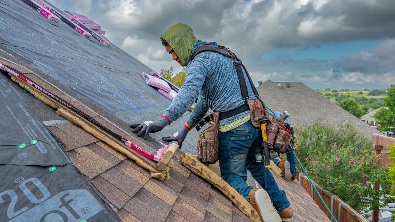 Roofer working a steep slope over synthetic underlayment as storm clouds build behind