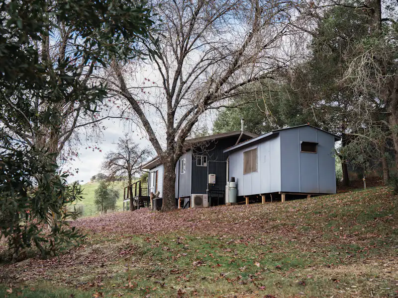 White farmhouse on an open rural hilltop behind a board fence and bare trees