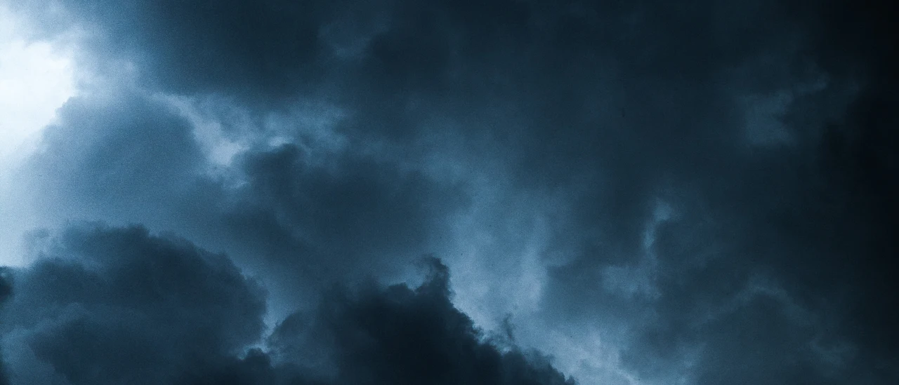 Deep navy storm clouds with light breaking through the center
