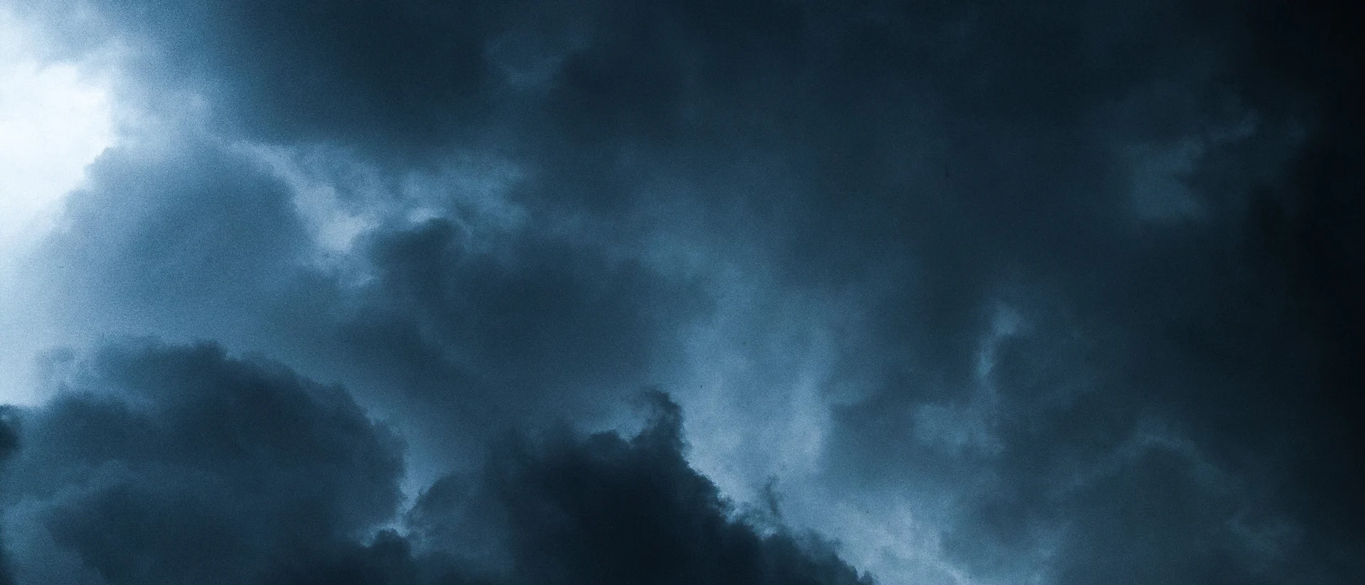 Deep navy storm clouds with light breaking through the center