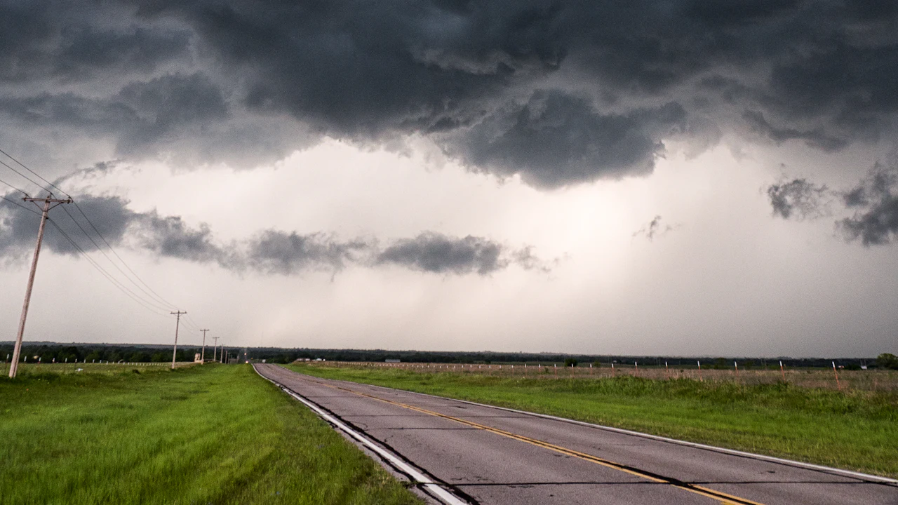 Heavy dark storm front over a rural two-lane road and open farm fields — representative