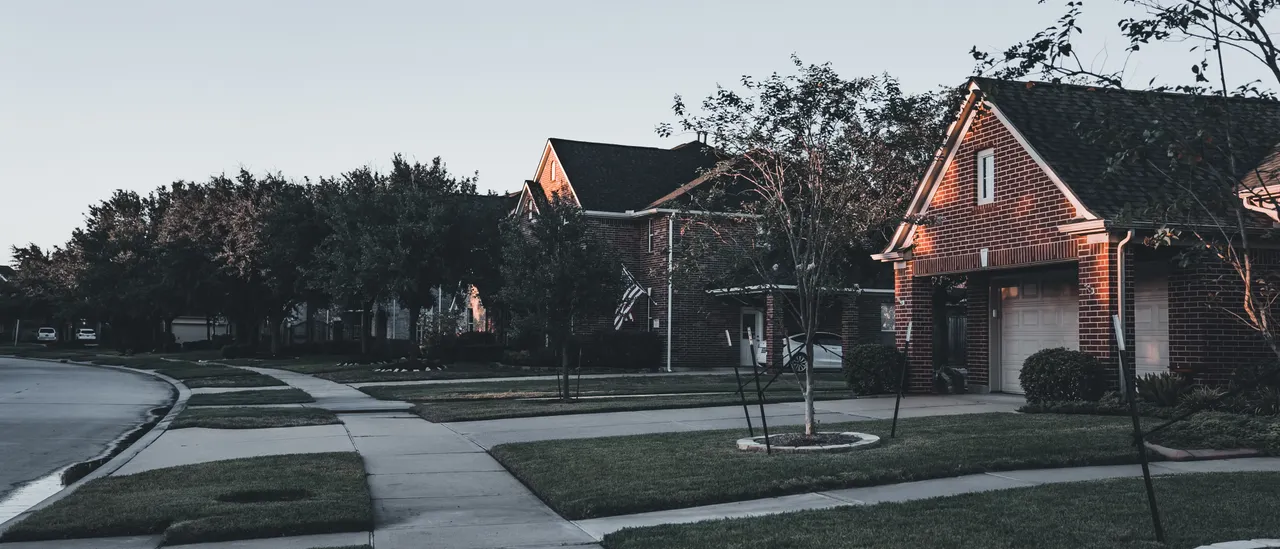 Quiet residential street of brick homes at dusk, rooflines fading into the evening sky