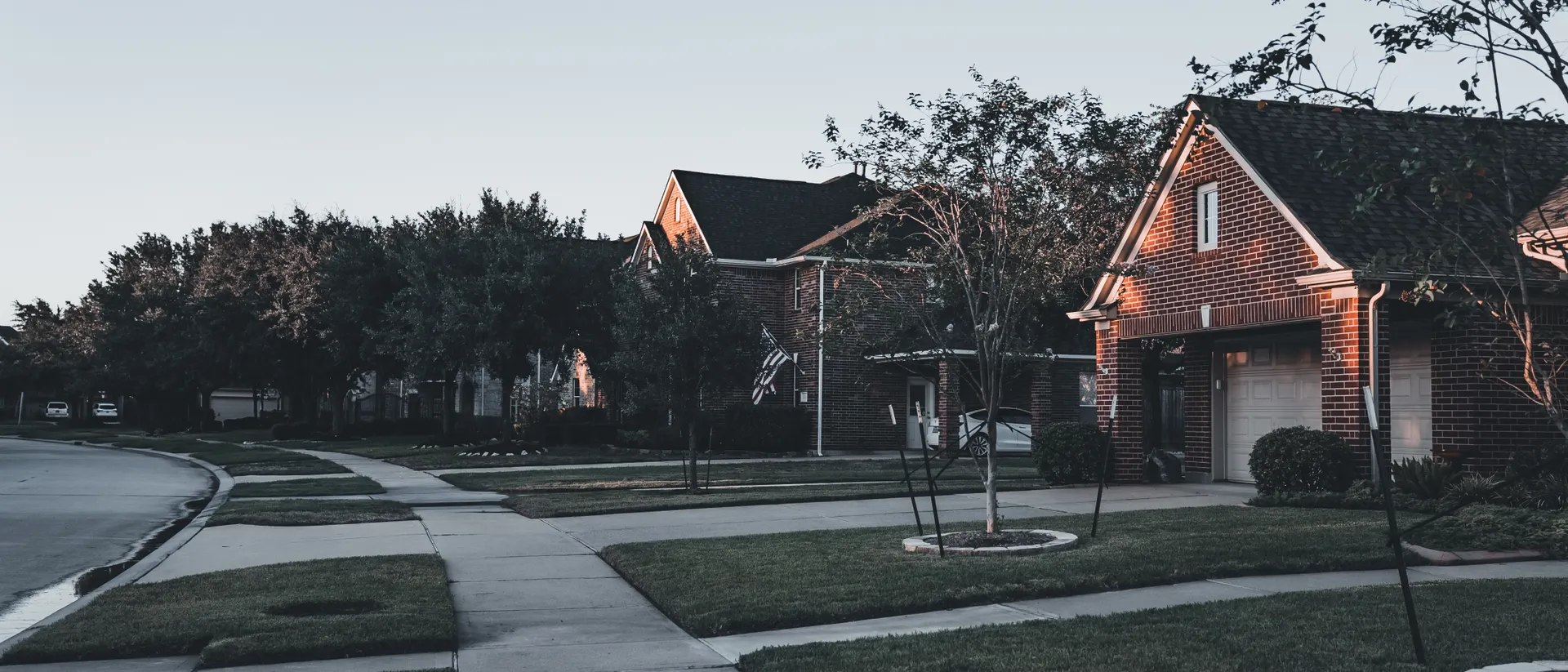 Quiet residential street of brick homes at dusk, rooflines fading into the evening sky