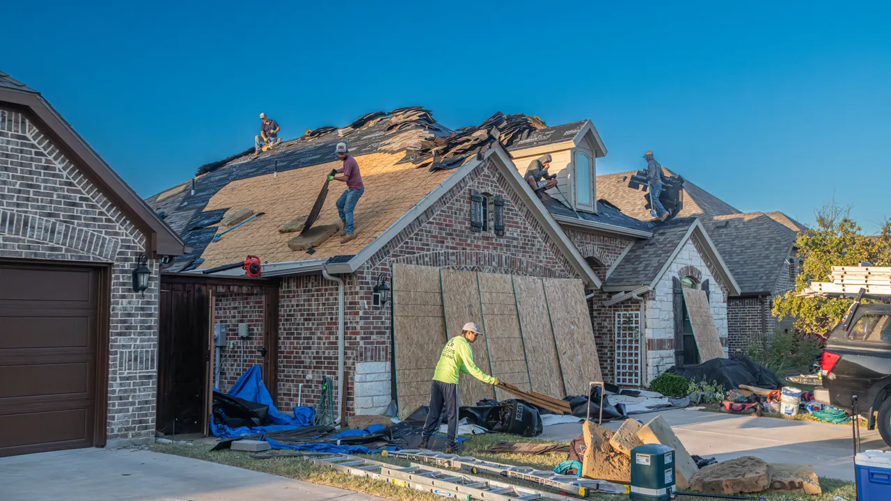 Tear-off in progress on a brick home, decking exposed, tarps protecting the landscaping below
