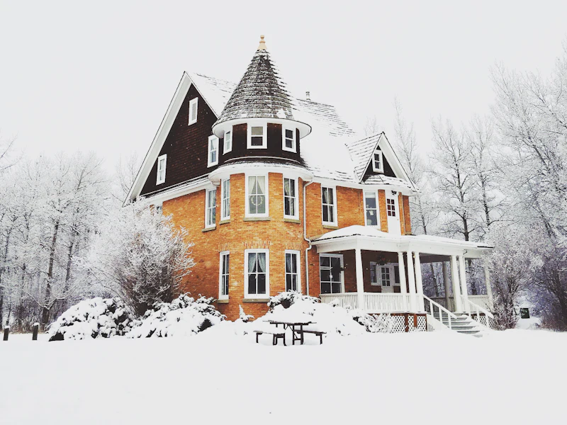 Brick Victorian farmhouse with turret and steep snow-dusted roof in open winter country