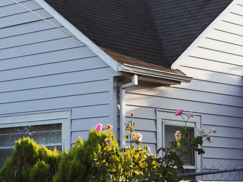 White-sided home with dark asphalt shingle roof, gutter and downspout at the eave